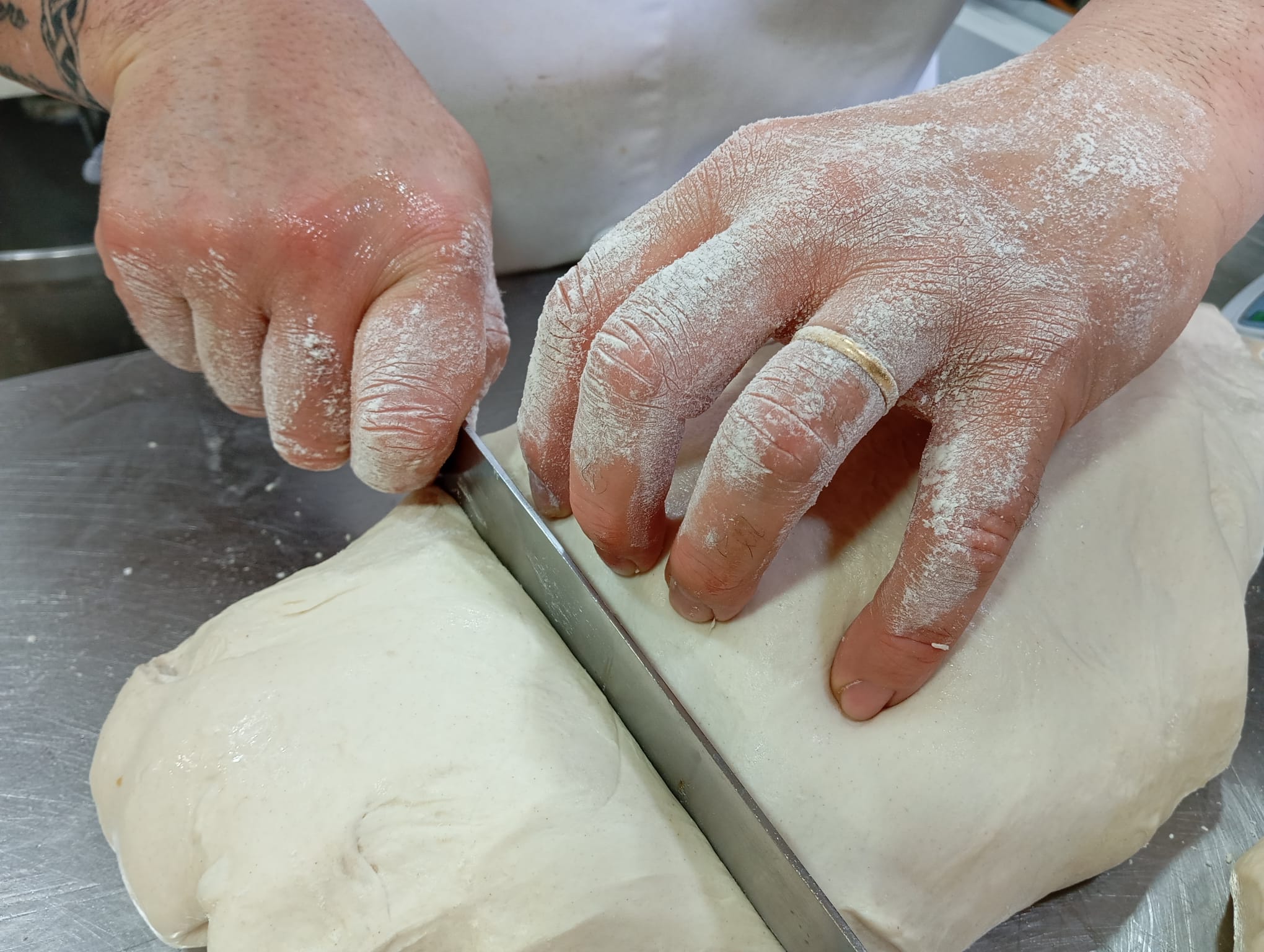 Elaboración artesanal de masa en el obrador (2) Manos de pastelero trabajando la masa con cuchillo sobre la mesa del obrador, proceso artesanal de pastelería.