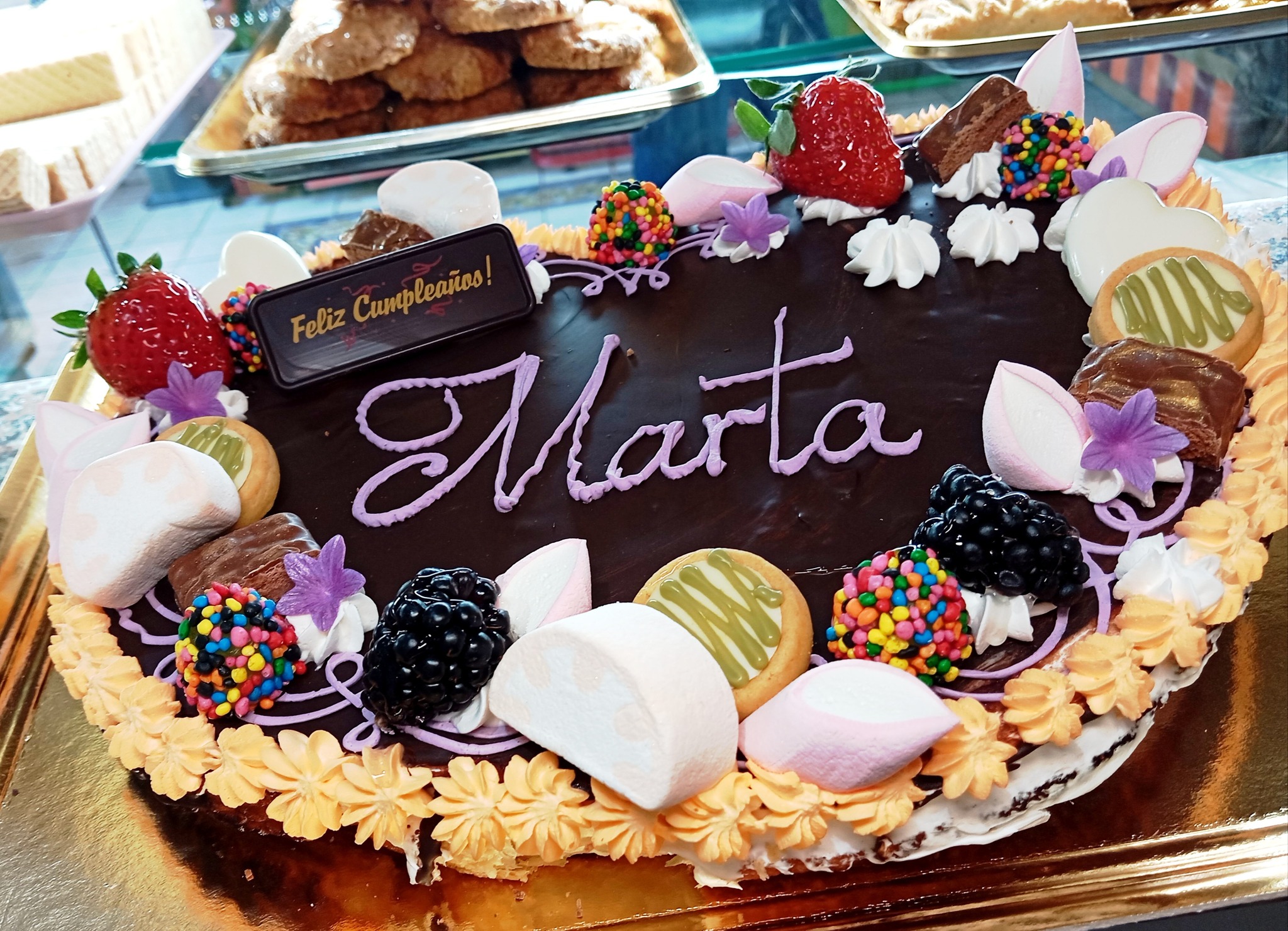 Palmera artesanal de chocolate personalizada para cumpleaños Palmera de hojaldre cubierta de chocolate y decorada con frutas, golosinas y el nombre Marta para una celebración de cumpleaños.