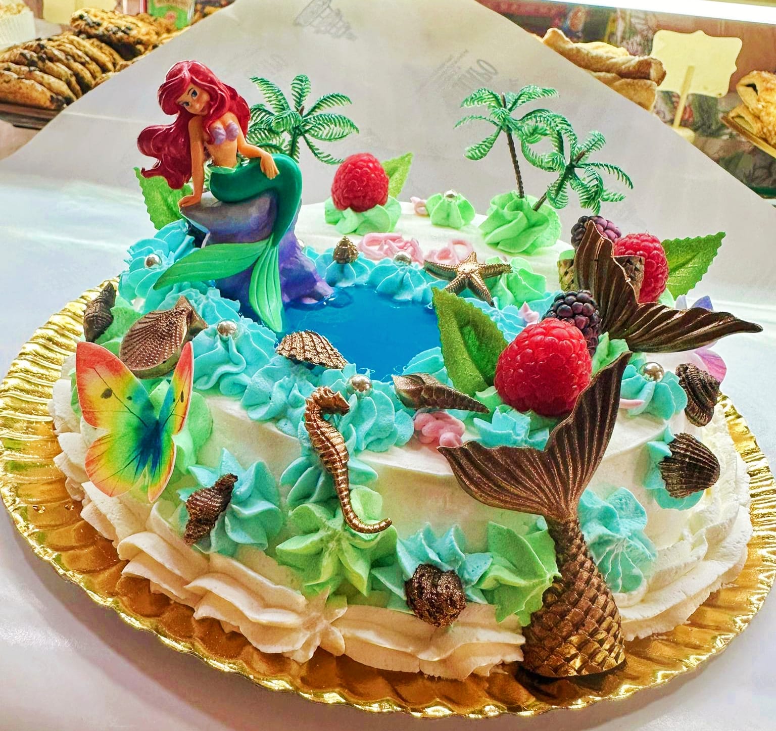 Tarta artesanal temática de sirena para celebraciones Tarta artesanal decorada con temática de sirena, con figuras marinas, colores azul y verde y detalles de frutas y chocolate.